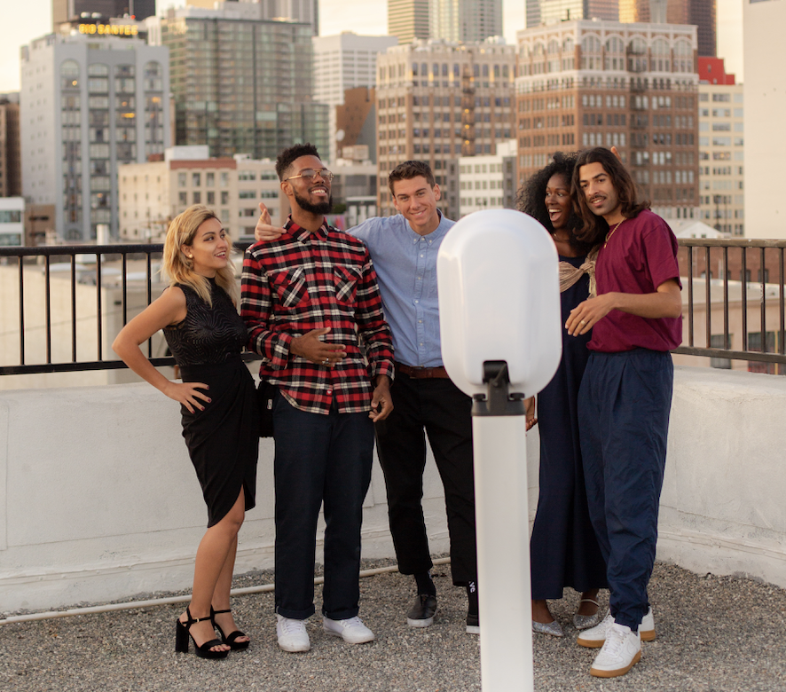 Friends laughing beside an open-air photo booth on a rooftop